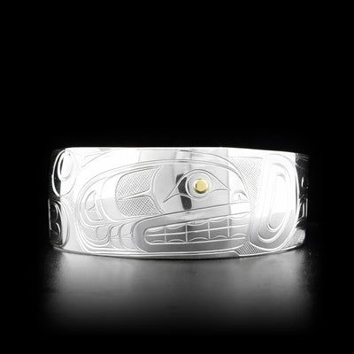 This silver and gold cuff bracelet is made from sterling silver and 14K gold and has a wide, slightly tapered band. There is a depiction of the Orca carved into the surface of the band and the eye of the Orca is made from 14K gold.