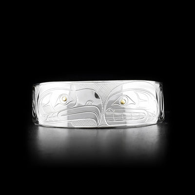 This silver and gold bracelet cuff is made from sterling silver and 14K gold and has a wide band with a gap in the back. There are depictions of the Eagle and the Orca carved into the surface of the band and the eyes of the Legends are made from 14K gold.