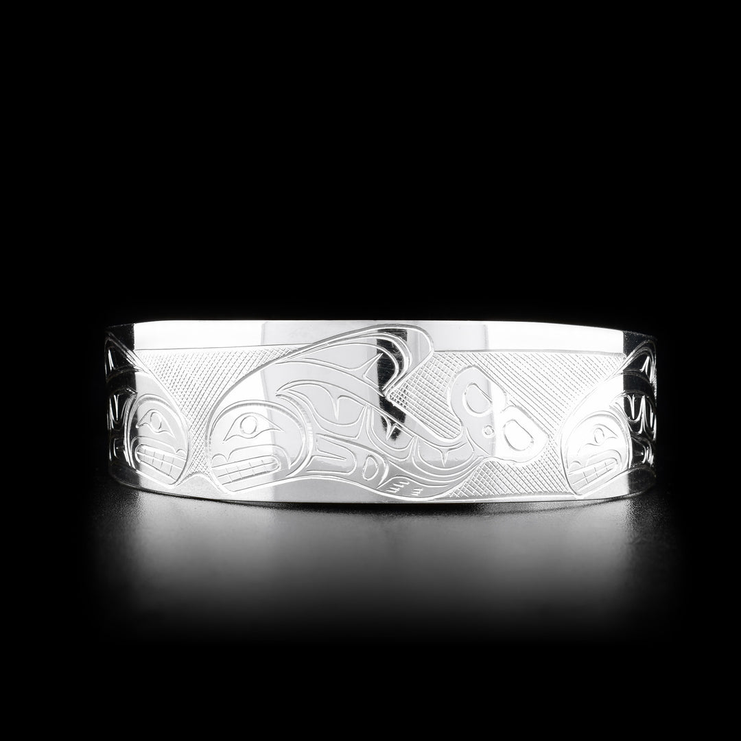 This Orca bracelet is made from sterling silver and has a wide band with a gap in the back. There are depictions of an Orca pod carved across the surface of the band.