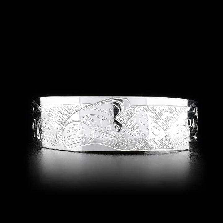This Orca bracelet is made from sterling silver and has a wide band with a gap in the back. There are depictions of an Orca pod carved across the surface of the band.