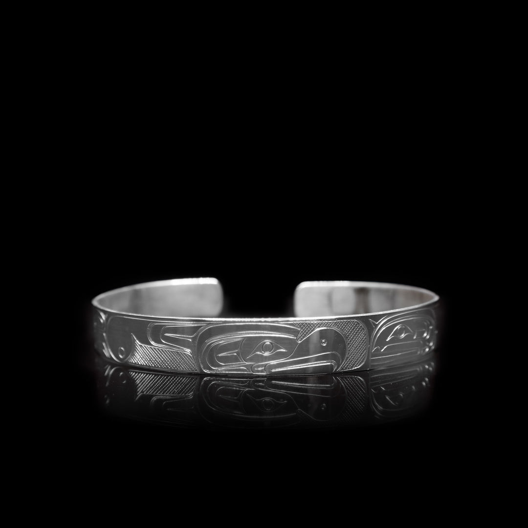 This sterling silver cuff bracelet a thin band with depictions of the Thunderbird and the Orca carved into the surface of it.