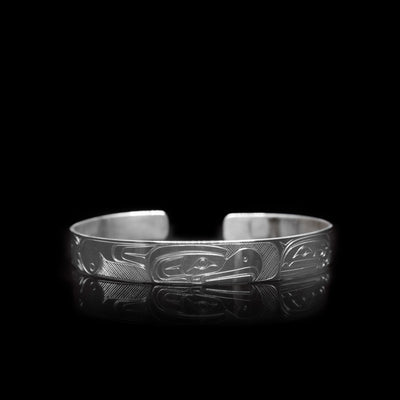 This sterling silver cuff bracelet a thin band with depictions of the Thunderbird and the Orca carved into the surface of it.