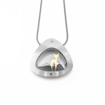 Rounded, triangular silver-coloured frame with gold-coloured cat standing inside. Grey and silver-coloured hills in background. Brushed and anodized aluminum. Minimalist design. Stainless steel snake chain included. By JR Franco.