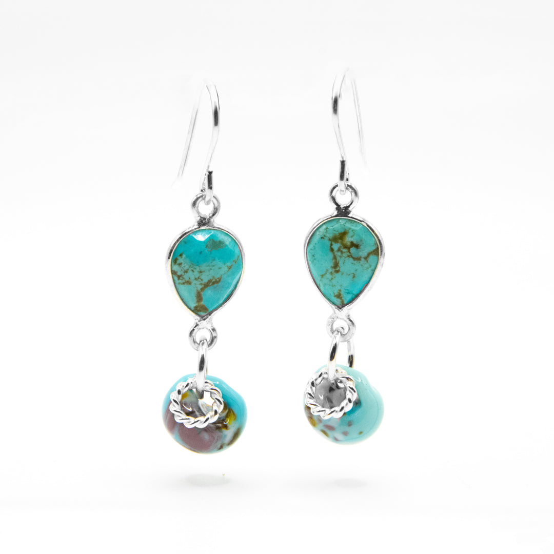 Faceted, downward teardrop-shaped turquoise dangles from hooks. Turquoise-like glass adornment and silver ring adornment dangle below gemstone. All metal is sterling silver.