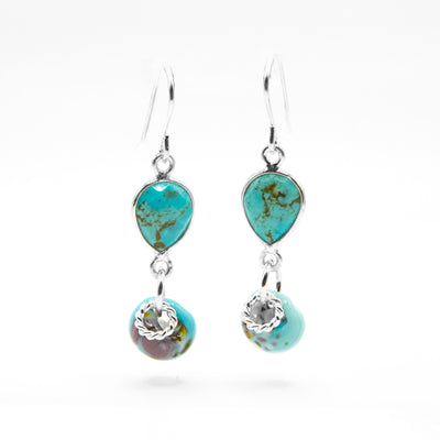 Faceted, downward teardrop-shaped turquoise dangles from hooks. Turquoise-like glass adornment and silver ring adornment dangle below gemstone. All metal is sterling silver.