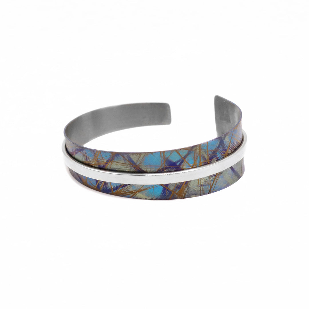 This tapered titanium bracelet cuff has been made using sterling silver and anodized titanium. There is a single, tapered titanium band with a gap in the back and a thin silver wire running through the center of the band. There are brilliant colored (gold, turquoise, purlpe) designs on the surface of the titanium that have been achieved by anodizing the metal.