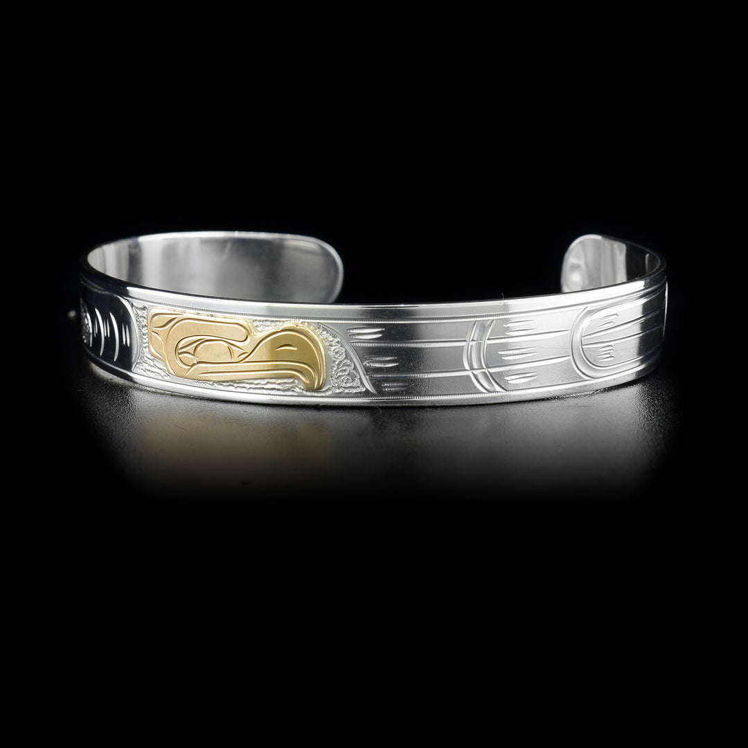 This gold and silver Eagle bracelet is made from sterling silver and 14K gold has a thin band with a depiction of the Eagle carved into it. The head of the eagle is made from 14K gold.
