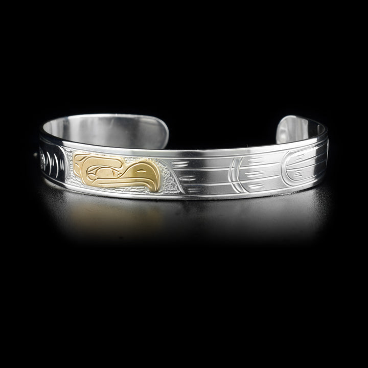 This gold and silver Eagle bracelet is made from sterling silver and 14K gold has a thin band with a depiction of the Eagle carved into it. The head of the eagle is made from 14K gold.