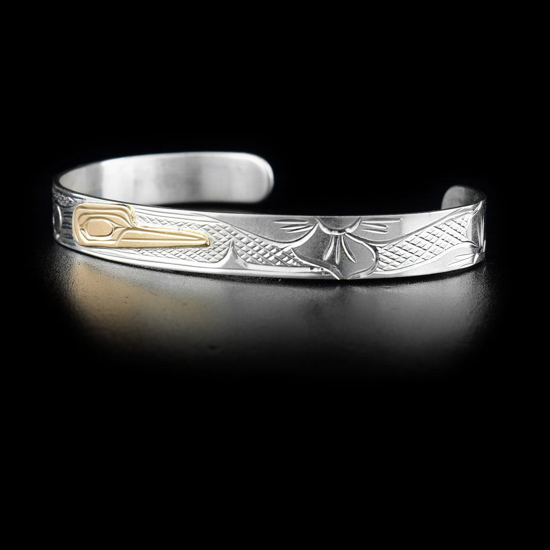 This small cuff silver and gold bracelet has a thin, sterling silver band with a depiction of the Hummingbird and a flower carved into it. The head of the Hummingbird is made from 14K gold. 