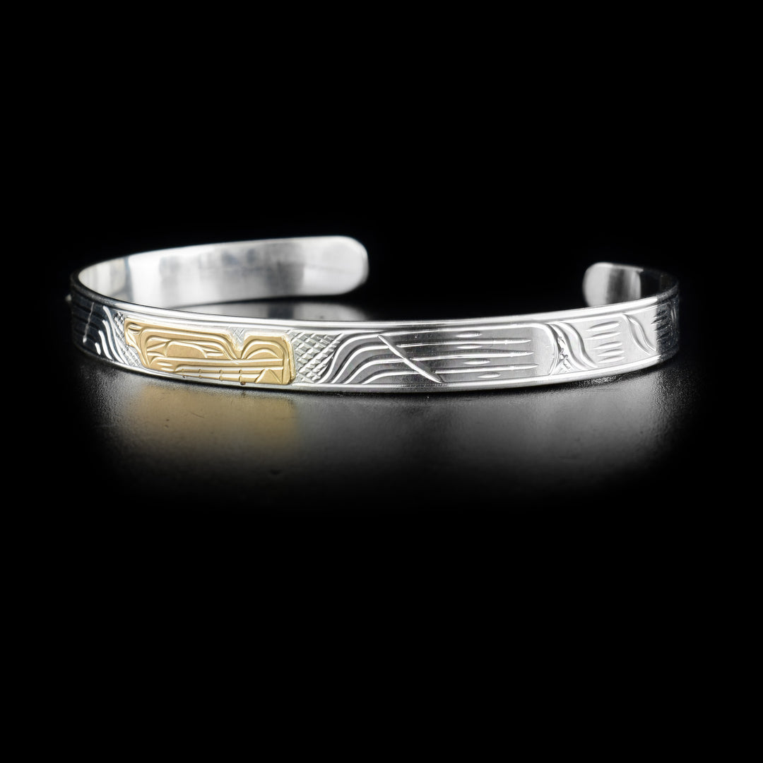 This sterling silver bracelet cuff has a thin band and carvings that depict the Wolf. The head of the Wolf is made from 14K gold.