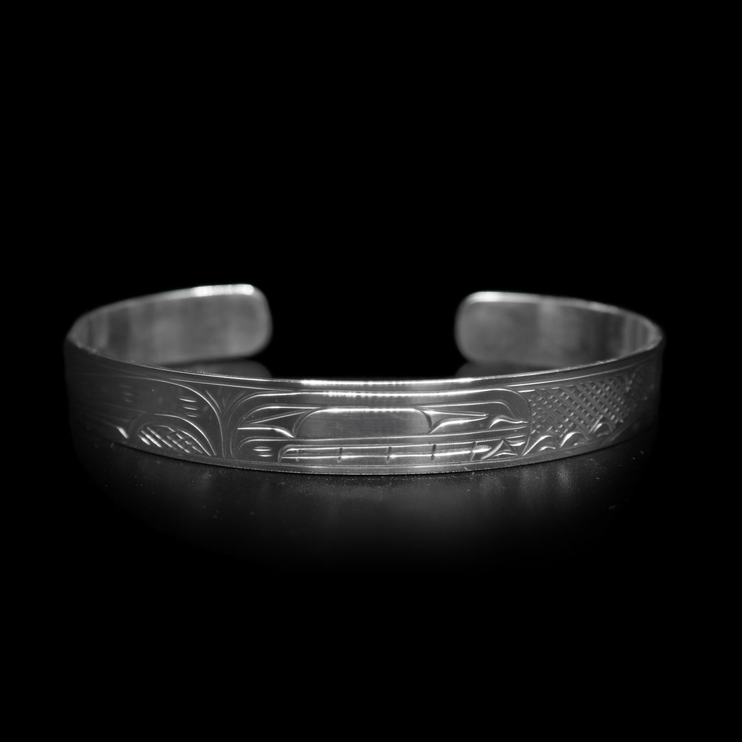 This dainty bracelet has a thin, sterling silver band with a gap in the back. The head of the Orca is carved in the center of the band and there are the backs of other whales with their dorsal fins breaching out of wave patterns. There are cross hatching patterns in the space behind the legends.