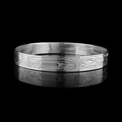This Salmon and Orca bracelet bangle is made from sterling silver and has a single, thin band. There are depictions of the Salmon and the Orca carved across the surface of the band.