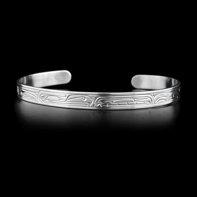 This sterling silver cuff bracelet is thin and has depictions of the Orca and the Thunderbird carved into it.