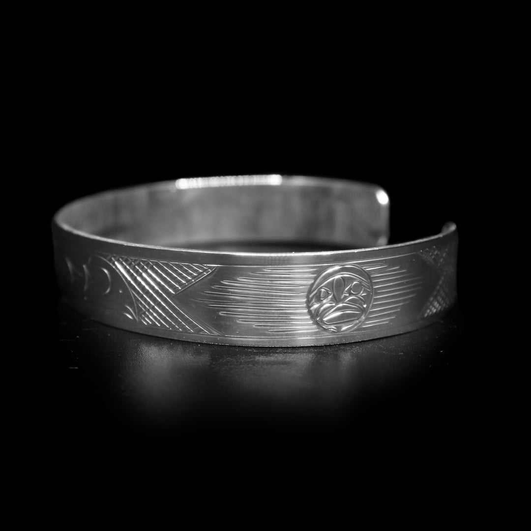This Raven bracelet has a single, sterling silver band with a gap in the back. There is a depiction of the Raven carved across the surface of the band and a small Sun carved in the side of the band.