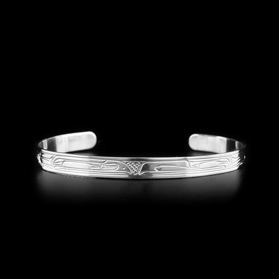 This sterling silver cuff bracelet has a thin band and is a cuff bracelet. There are depictions of the Raven and the Thunderbird carved into the surface of the band.