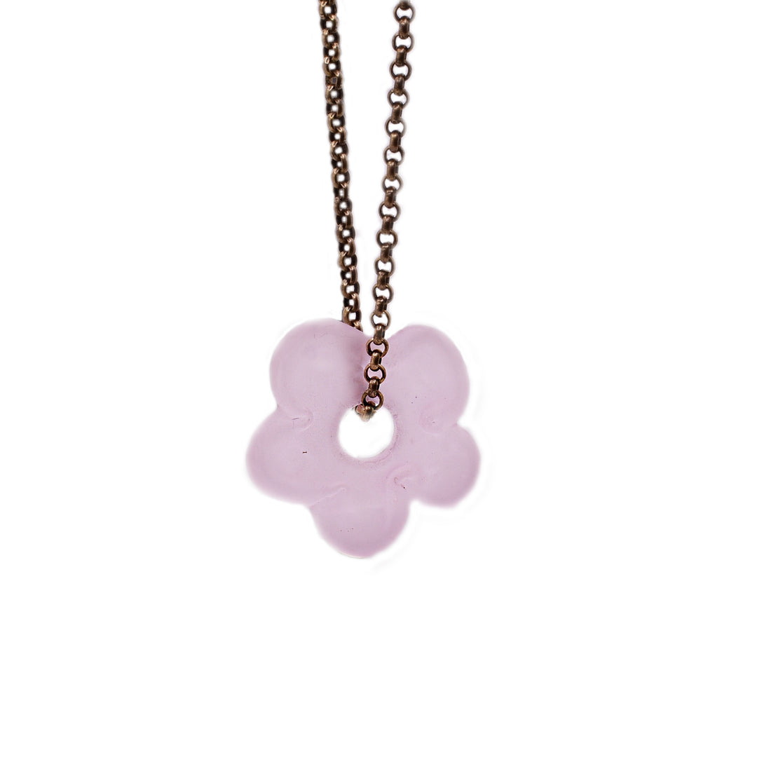 Thick, brass belcher chain with flat, light pink, matte glass flower pendant. Pendant has large, circular opening in center that chain goes through.