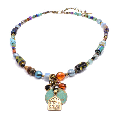 This glass bead necklace is made from brass, lampworked glass beads, pearls, amethyst, lapis, and turquoise. There are dangling pendants made from brass and gemstones attached to a jump ring on the necklace.