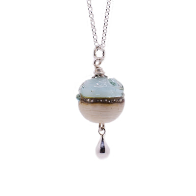 This necklace has a dainty sterling silver chain. The pendant is a small glass bead that resembles a beach and water and has a silver teardrop at the bottom of it.