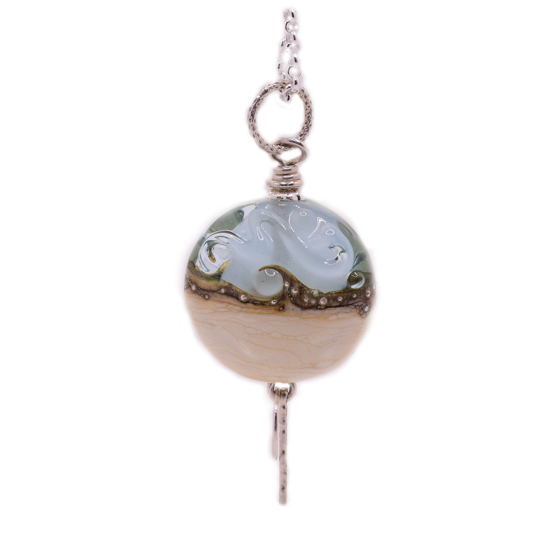 This sterling silver by the sea glass necklace has a dainty cable chain. The pendant is a large, colorful glass bead with a silver pin going through it.