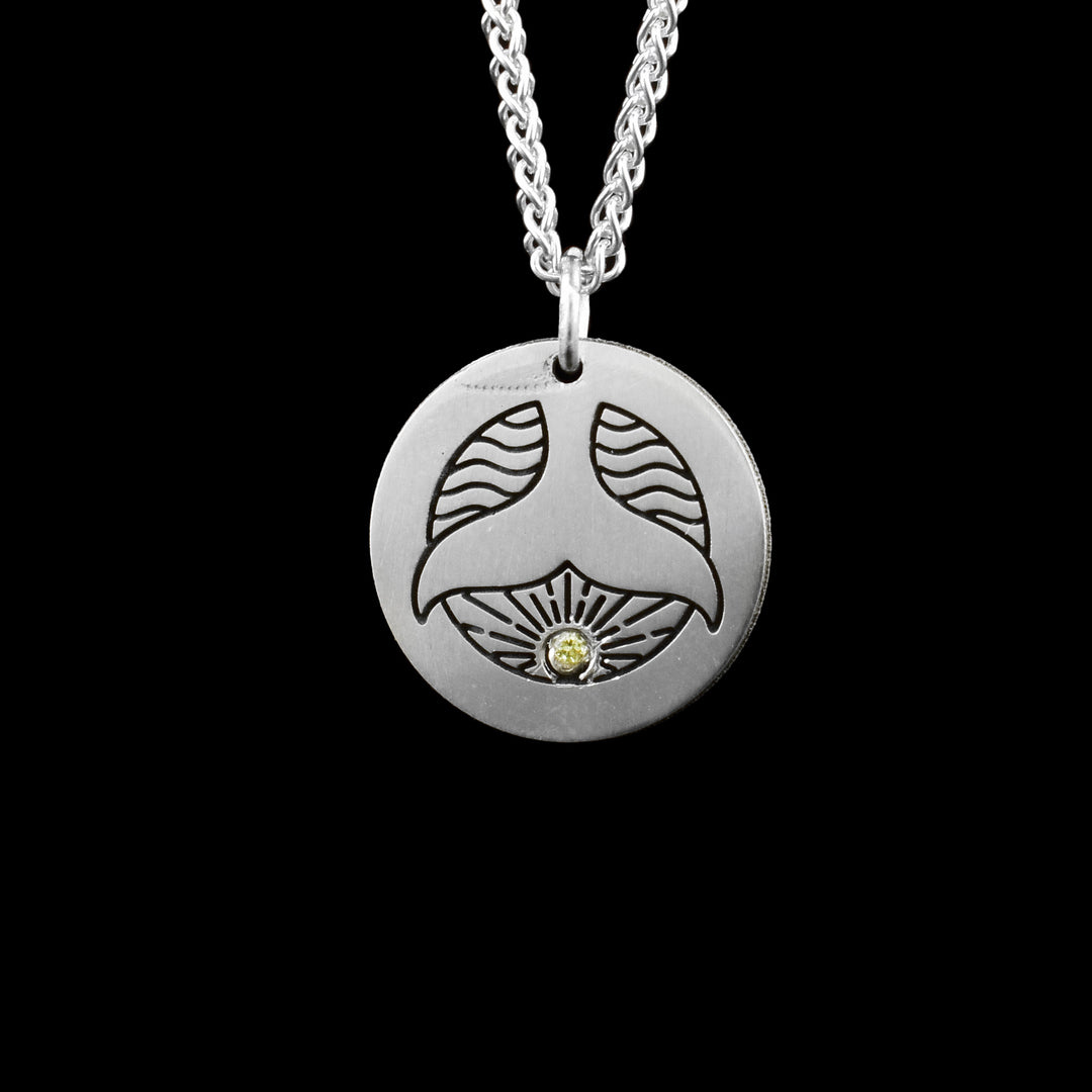Whale Tail Pendant, a dainty circular silver pendant is etched with a wavy texture to represent the ocean and a whale tail over top making a beautiful west coast design. under the whale is a yellow gemstone.