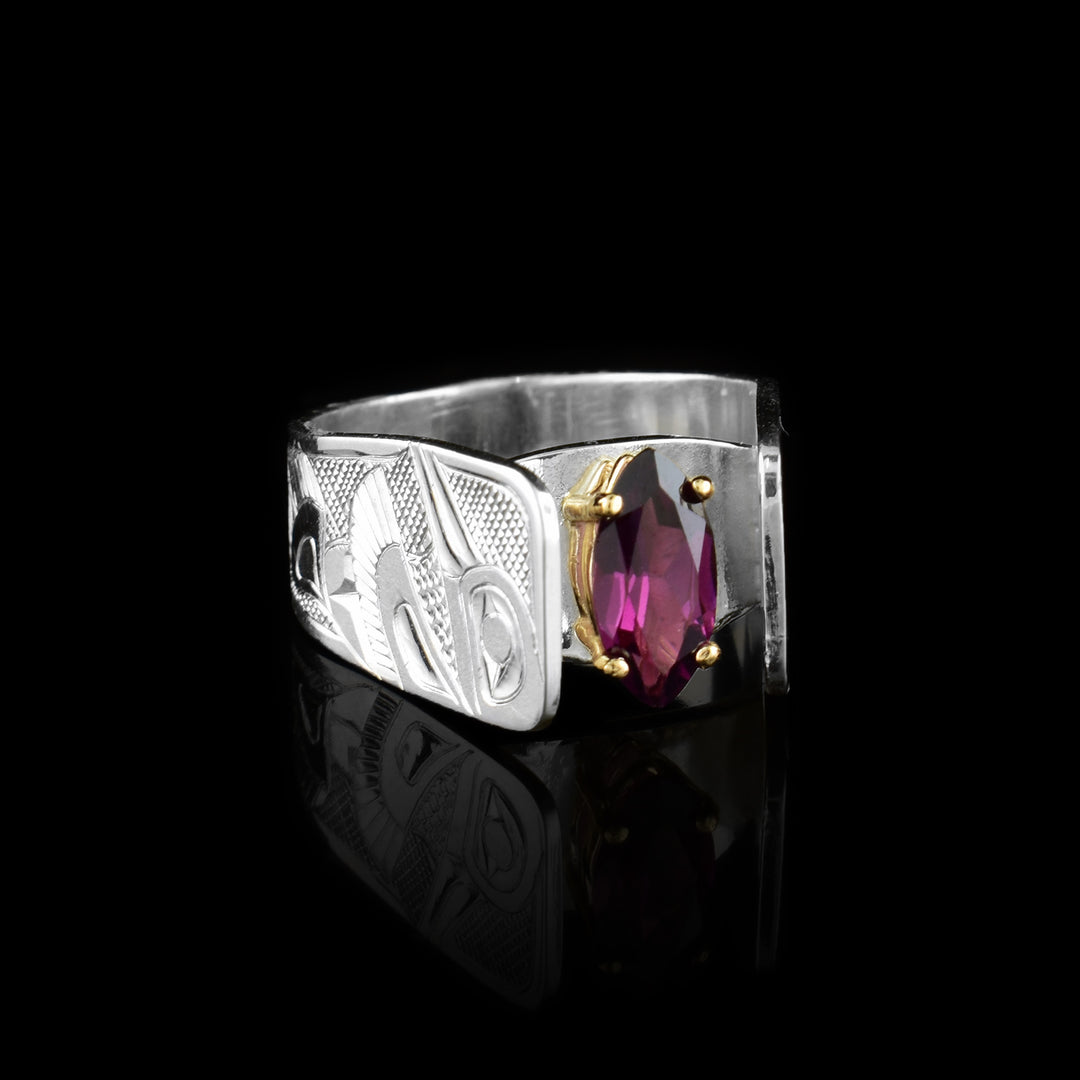 This wide Hummingbird ring has been hand carved by Tlingit artist Fred Myra. There are full body depictions of the Hummingbird legend carved into the sterling silver band of this marquis cut garnet solitaire ring.