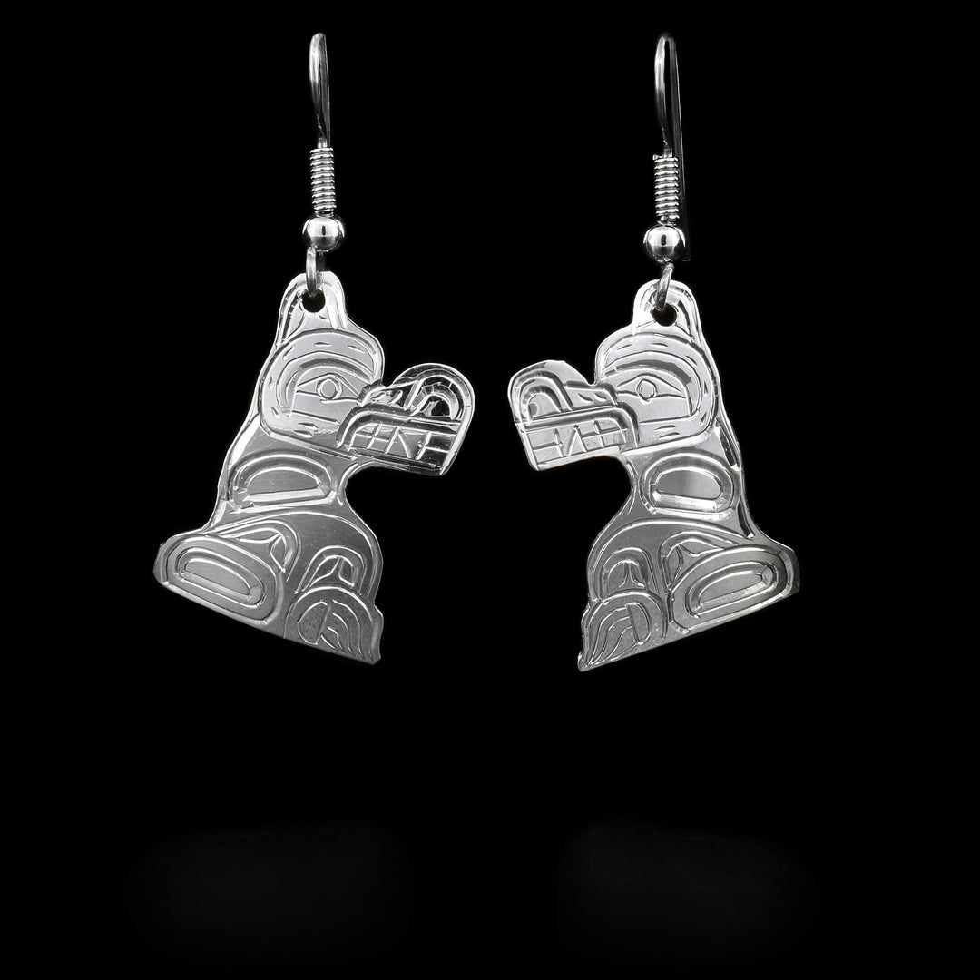 These Bear earrings have hooks which have Bear-shaped hangs attached to them with a jump-ring. The Bear is shown at a side profile and has a long snout with its teeth exposed. The details of the Bear are carved into the hangs. The earrings are sterling silver.