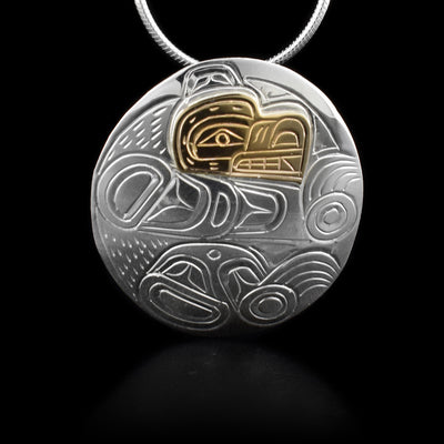 This sterling silver and 14K gold pendant is oval shaped and has a depiction of the Bear carved into it. The Bear's face is made out of gold.