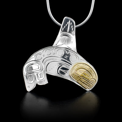 This silver and 14K gold pendant is shaped like the Orca and has carvings that depict the Orca. The face of the Orca is made of 14K gold.