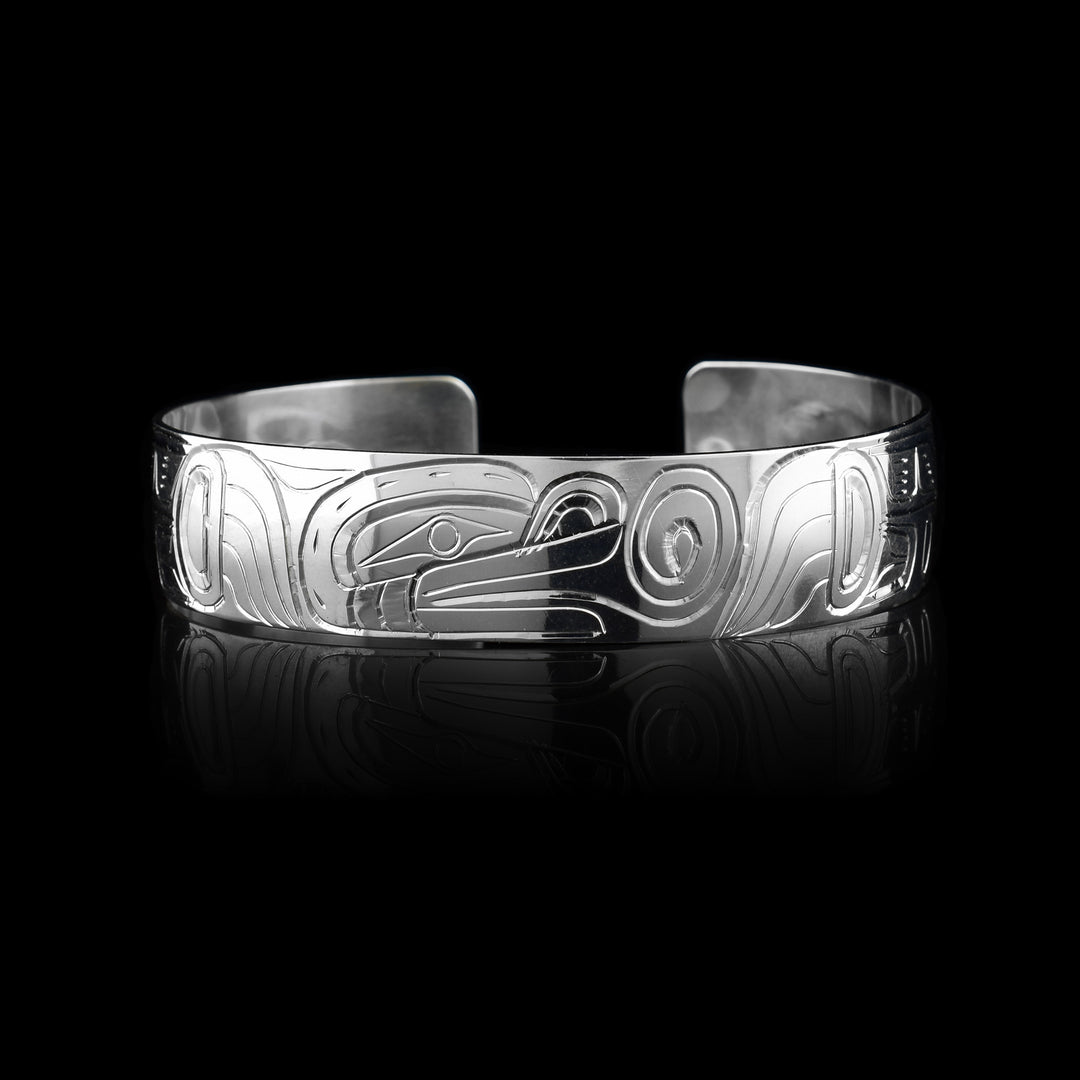 This elegant Frog bracelet cuff has a single, sterling silver band with a gap in the back. The head of the Frog is carved at a side profile in the center of the band. It is facing the right and has its tongue extending form its mouth with a spiraling curl at the end. On either side of the band the rest of the legend is depicted with its legs held at its side and having circular and triangular designs on the surface of them.