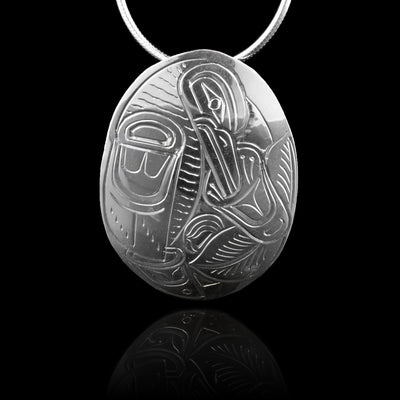 This Raven pendant has a wide, oval shape and is made form sterling silver. There are carvings on the piece depicting the Raven legend eating from a flower on it.