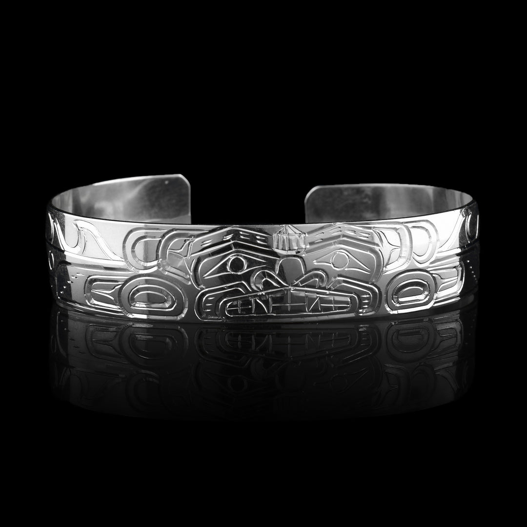 This sterling silver cuff bracelet has a single band with a depiction of the Sisiutl which is an indigenous sea serpent that has been carved into the surface of the band. The head of the serpent is in the center and around the band there is a serpent body with ridges on the top of it.