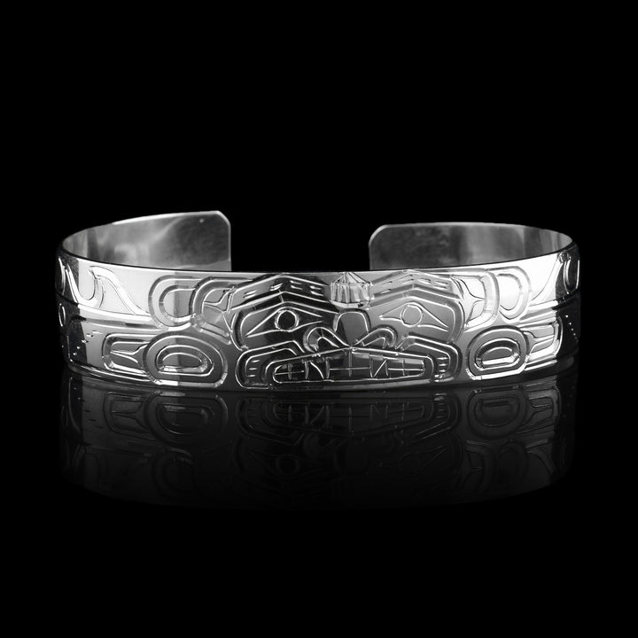 This sterling silver cuff bracelet has a single band with a depiction of the Sisiutl which is an indigenous sea serpent that has been carved into the surface of the band. The head of the serpent is in the center and around the band there is a serpent body with ridges on the top of it.