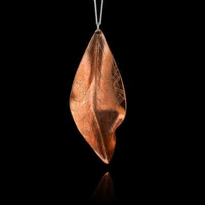 This leaf pendant necklace is made from copper and has a dainty sterling silver chain with a leaf shaped pendant. The pendant is copper and has folds and designs on the surface of it depicting a realistic leaf.