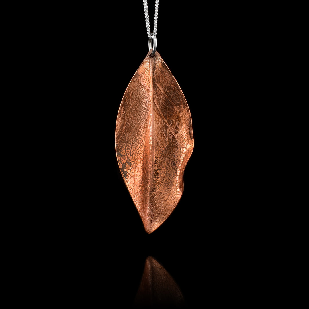 This leaf pendant necklace is made from copper and has a dainty sterling silver chain with a leaf shaped pendant. The pendant is copper and has folds and designs on the surface of it depicting a realistic leaf.
