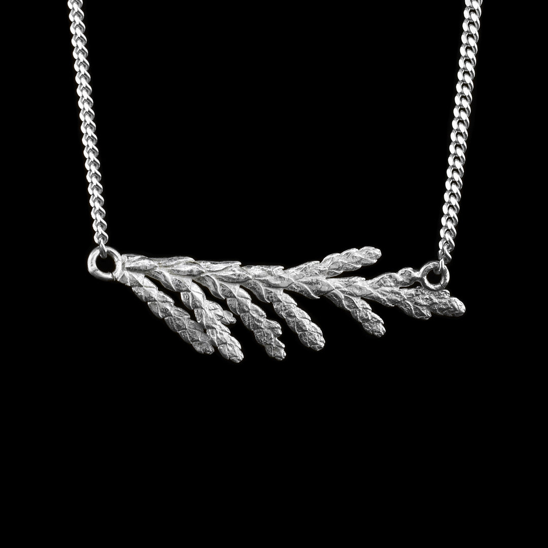 This cedar branch necklace is made from sterling silver and has a realistic cedar needle branch pendant. The pendant is held horizontally between the chain.