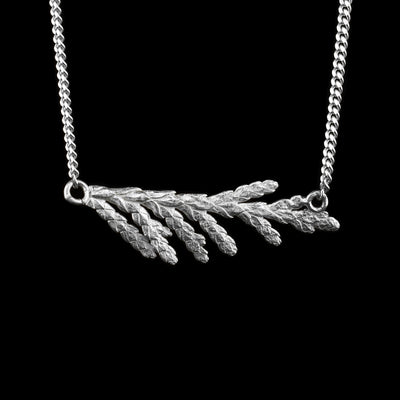 This cedar branch necklace is made from sterling silver and has a realistic cedar needle branch pendant. The pendant is held horizontally between the chain.