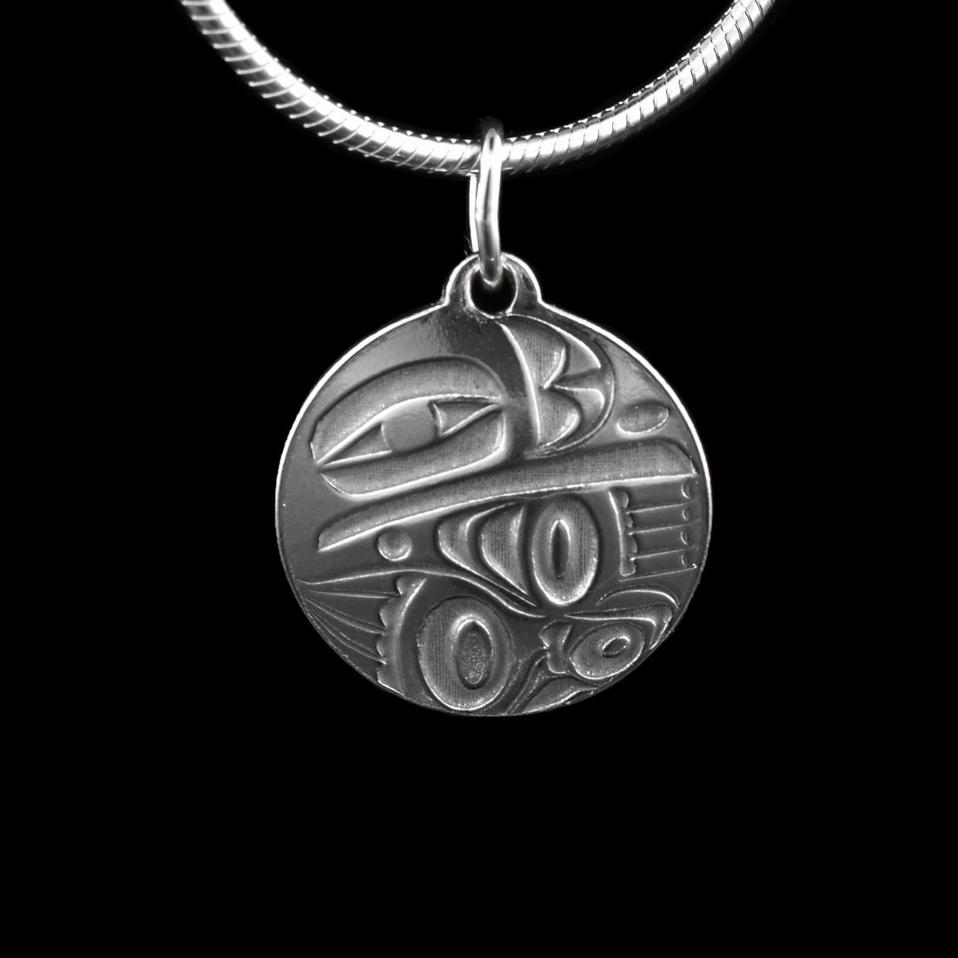This dainty Raven sterling silver pendant has a circle shape made from sterling silver. There is a depiction of the Raven cast into the pendant at a side profile. The top half consists of the eye, beak and nose and below is a wing design with feather details included.