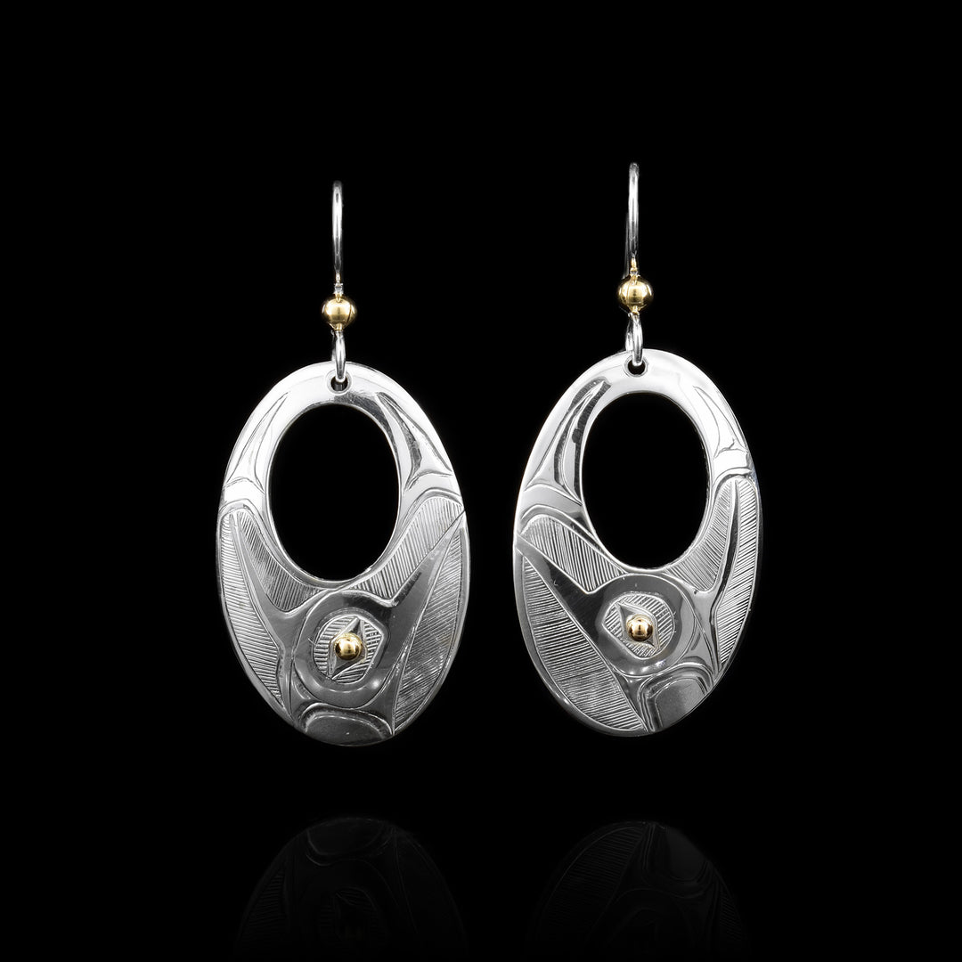 These dangling silver and gold oval Hummingbird earrings. The earrings surface is all sterling silver carved with the hummingbird legend. The eye of the bird is 14k gold.