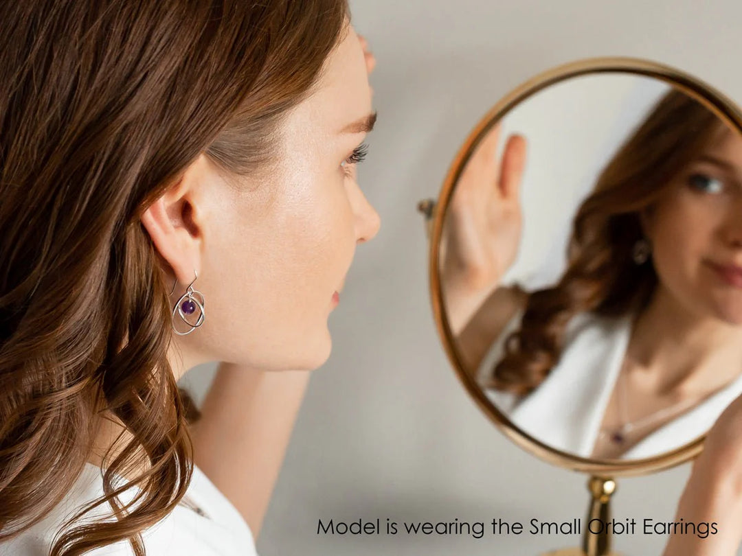 The model wears the earring and the photo is taken from the back to display the ear. The model looks into a mirror to show the front of her face.