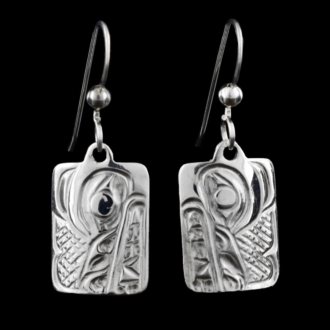 These silver earrings that are rectangle dangling features a detailed wolf design, inspired by Indigenous art. The carved pattern shows the wolf’s eye and face using traditional shapes and lines.
