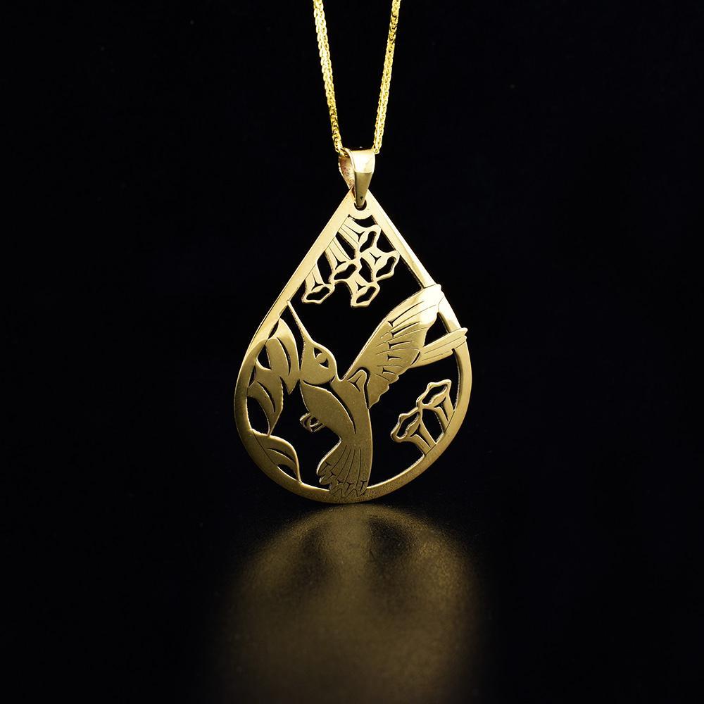 This 14K gold Hummingbird pendant has a large, teardrop shape. The piece has cutout designs depicting the Hummingbird among flowers.