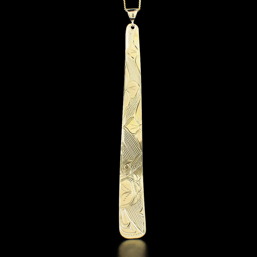 14K Gold 4" Tapered Hummingbird Pendant by Victoria Harper. The design depicts a hummingbird in the bottom left corner of the pendant feeding from a flower. The hummingbird has its wing spread out and underneath you can see the tail. Above the hummingbird there are 2 more large flowers. The background has been neatly hand-carved in a crisscross pattern to allow for the hummingbird and flowers to stand out.
