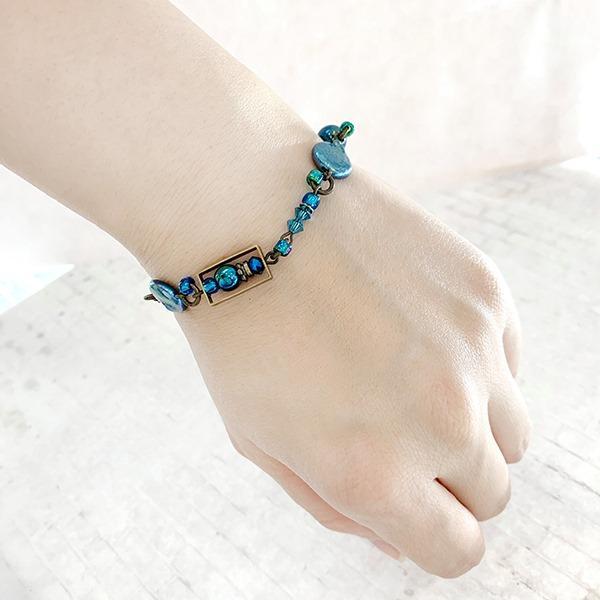This blue crystal bead bracelet is made from brass, Swarovski crystal, freshwater pearls, and glass. The beads are different shapes and sizes and made from all of the listed materials.