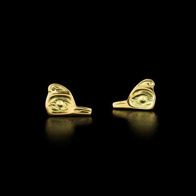 14K Gold Cutout Hummingbird Cast Studs by Carrie Matilpi. Each earring is in the shape of a hummingbird's head. The hummingbird has a large, open eye with a small beak pointing inward and a small feather on the top of its head.