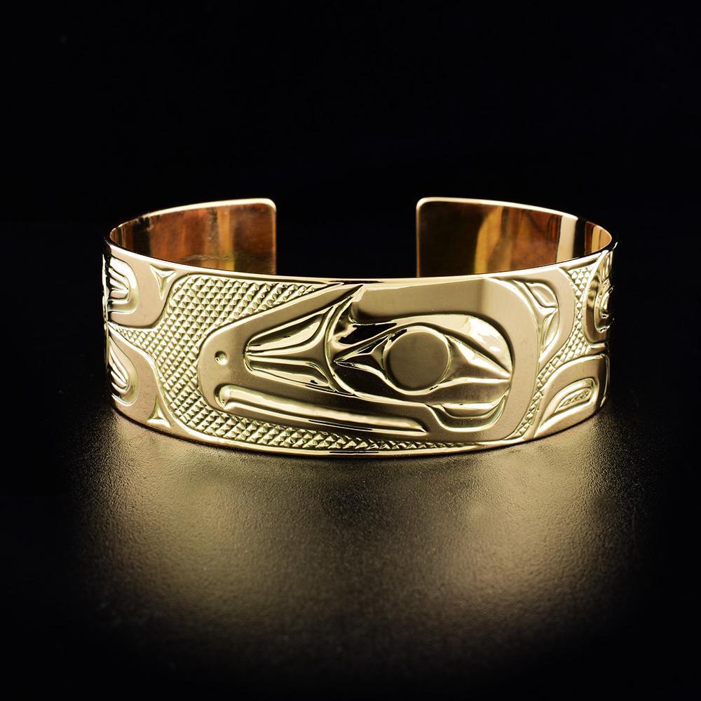 This 14K gold cuff bracelet has a single, wide band with a gap in the back. There are depictions of the Sun and the Raven carved into the surface of the band.