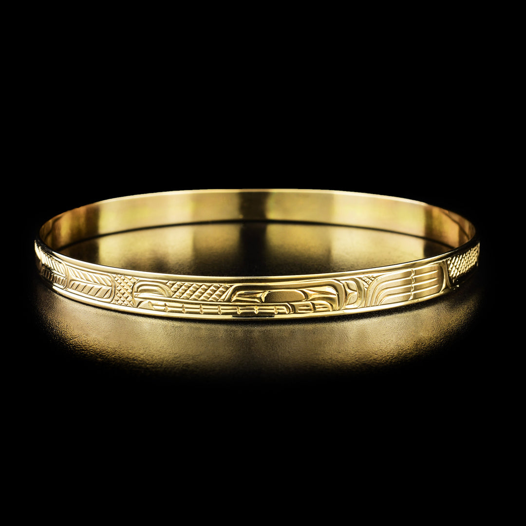 14K Gold 1/4" Wolf and Moon Bangle by Charles Harper. The design of this bracelet depicts the profile of a wolf's head with a long, narrow snout facing towards the left in the center of the bracelet. To the left of the wolf's head, the artist has hand-carved a small moon. Along the rest of the bracelet the artist has hand-carved intricate designs representing the moon's ring and the wolf's fur.