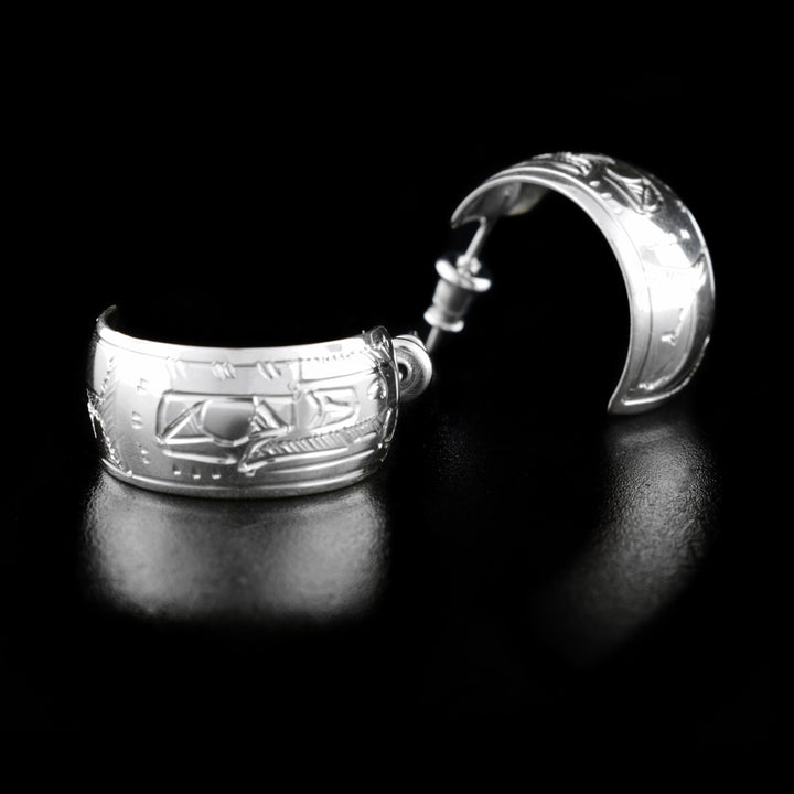 These wide hoop earrings are made form sterling silver and have wide bands curved into hoops with a gap in the back. There are depictions of the Raven carved into the surface of the band.