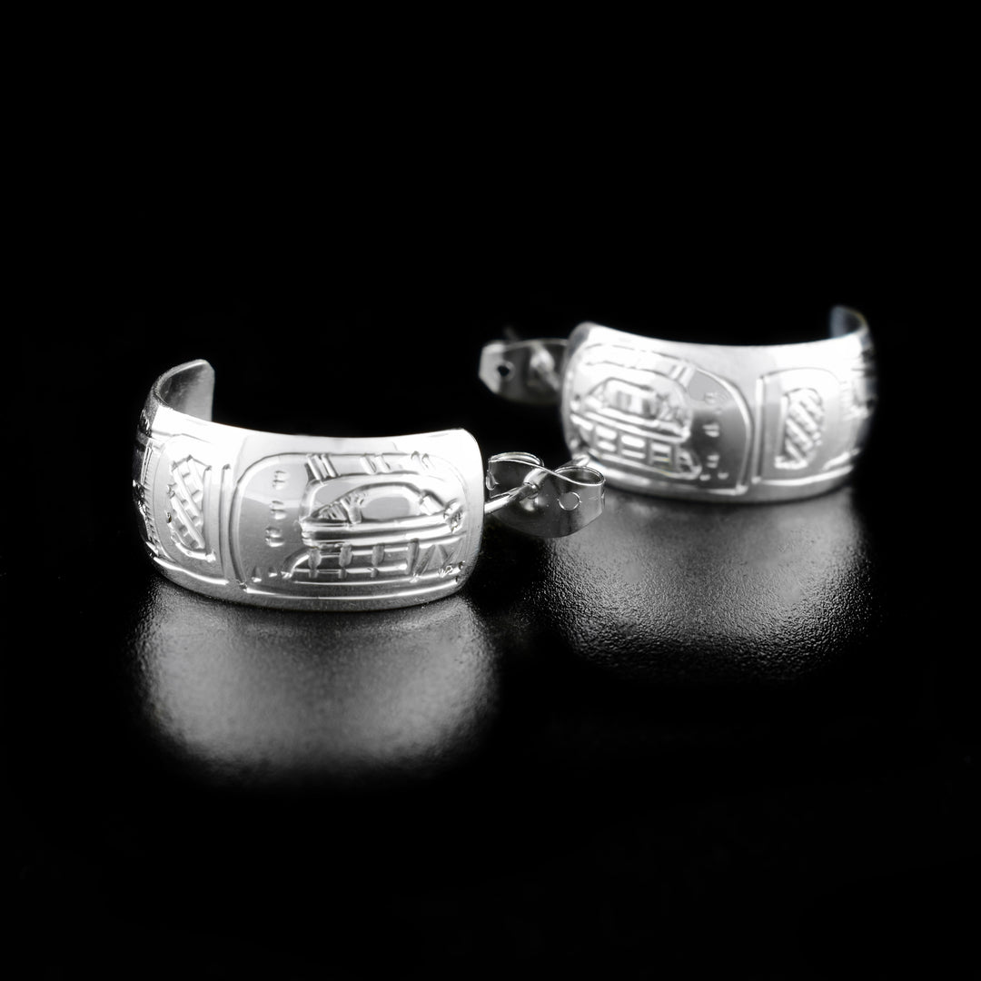 These Orca earrings are made from sterling silver and have small hoops with a wide band. There are depictions of the Orca carved into the surface of the hoops.