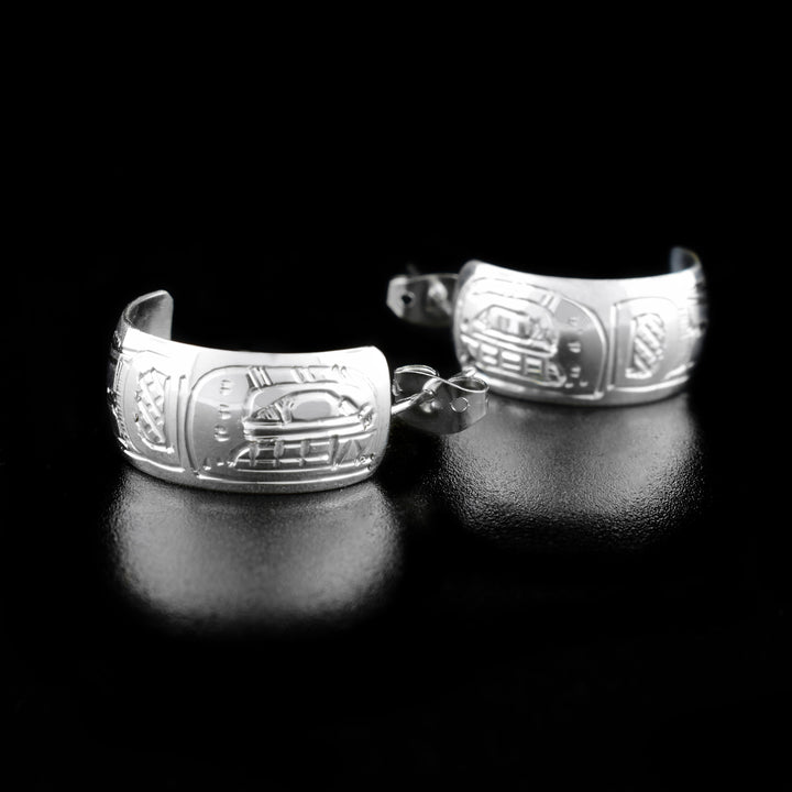 These Orca earrings are made from sterling silver and have small hoops with a wide band. There are depictions of the Orca carved into the surface of the hoops.