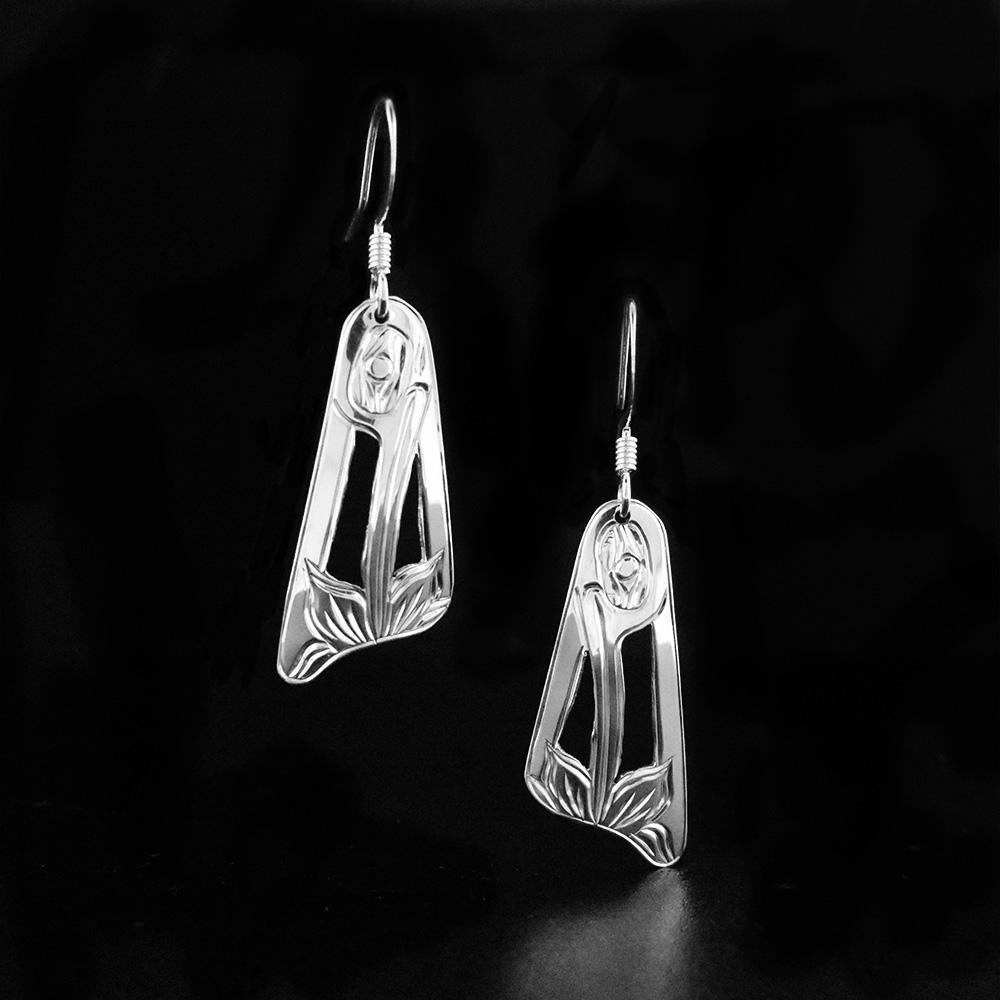 These dangling Hummingbird earrings are made from sterling silver and have wide, tapered hangs. There are cutouts and carvings on the surface of the hangs that depict the Hummingbird.